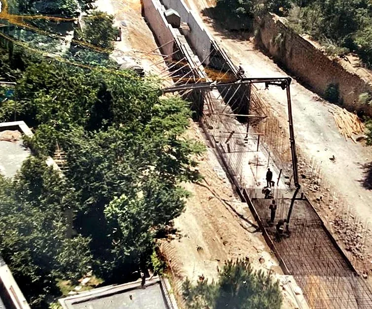 Aerial view of a sloping site with a new road cut, a long retaining wall, steel reinforcement on the ground and trees on either side.